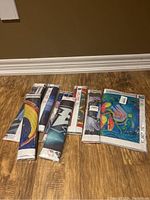 Eight rolled and sealed diamond art kits laid out on wood floor showing varied colorful designs.