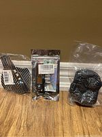 Three items still in original packaging arranged against a wall on wooden floor: carbon fiber style door stickers, BMW keychain in holographic pouch, and rhinestone black steering wheel cover.