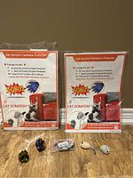 Two packages of cat scratch furniture protectors each showing included items and usage graphics with a cat image on box. Four small cat toys placed in front including colorful balls and small mice.