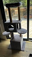 Front view of grey cat scratch stand with two vertical scratching posts, cubed hideaway, and round platforms.