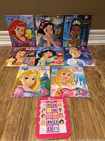 Photo showing 8 Disney Me Reader books with covers featuring Ariel, Snow White, Tiana, Belle, Jasmine, Rapunzel, Aurora, and Sleeping Beauty. A pink electronic Disney Me Reader device is placed in front.