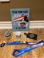 Full view of all items including metal sign, ship model, collectible tin, luggage tag, and lanyard displayed on floor against wall.