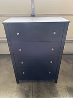 Front view of a brown wooden chest with four drawers and silver round knobs, standing on a concrete floor.
