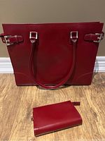 Red leather Franklin Covey briefcase handbag with double handles and matching small zipper pouch placed on floor