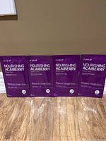 Four purple Glam Up Nourishing Acai Berry face mask packets displayed side by side on a wood floor.