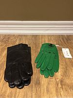 Pair of black and green gloves placed flat on a wooden floor to show overall look and color.
