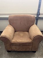 Front view of the small tan upholstered armchair showing its shape, cushion, and armrests.