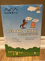 Front of sealed package showing the product name, brand Numeta, and cartoon animal illustrations highlighting features such as dry erase, strong magnets, weekly/daily records, and ability to stick on the fridge.