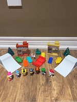 Overview of all items including two snow ramps, several colorful chairs and tables, two storefront play sets, three Christmas trees, and seven Paw Patrol character figurines arranged in front.