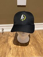 Front view of black snapback hat showing the embroidered white witch silhouette inside a yellow crescent moon.