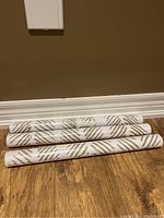Three rolls of new peel and stick wallpaper on wooden floor, showing their length and pattern.