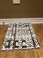 Nine rolls of peel and stick wallpaper featuring a black bamboo leaf pattern on white background, laid on wooden floor.
