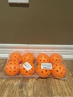 Two unopened packs containing a total of eight bright orange pickleballs, each with multiple small holes.