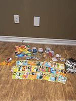 Full lot overview showing the assortment of Pokemon cards, character balls, pins, patches, sticker packs, and book spread on floor.