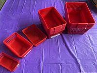 Five red plastic baskets in descending size order placed on a purple surface, showing the collection and size variations.