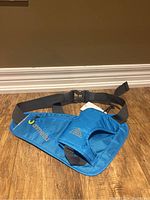 Full view of the blue running belt laid out, showing the water bottle holder on one side with an elastic strap and the zipper pouch on the opposite side, attached with an adjustable black strap and plastic buckle.