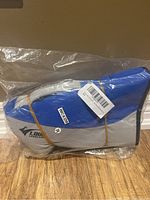 Side view of blue and grey dog life jacket in sealed plastic bag showing brand tag and size sticker M.