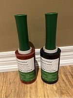 Two rolls of stretch wrap with green handles, one red wrap and one black wrap, standing upright on floor.