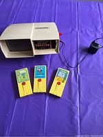 Photo showing the vintage Fisher Price Movie Viewer Theater and three yellow plastic movie cartridges featuring various Disney movies, with power adapter.