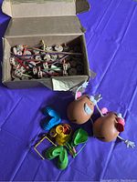 Photo showing a box of vintage wooden Tinker Toys pieces and two vintage Mr. Potato Head figures with assorted plastic parts.