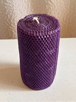 Single cylindrical purple beeswax candle with visible wick on top and honeycomb surface texture, placed on a flat white surface with neutral background.