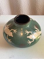 View of green clay pot with white frog designs, showing rounded shape and narrow mouth.