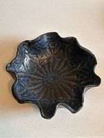 Top-down view of the handmade dark glazed pottery bowl with irregular wavy rim and carved floral-like pattern inside.