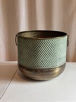 Front view of large metal plant holder showing perforated upper section and solid base with side handles.