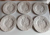 Top view of six white ceramic plates with detailed maple leaf patterns, arranged in two rows on a white surface.