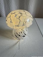 Side view of the glass mushroom lamp showing white dot patterns on the cap and white swirl patterns on the stem, plugged in and lit.