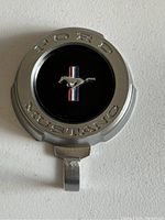 Photo of the first Ford Mustang emblem coat hanger showing chrome round badge with Mustang horse logo and hook below.
