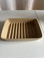 Small beige rectangular stoneware baking dish with ridged base shown from above and side views.