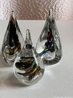 Grouped front view showing three teardrop-shaped clear crystal glass sculptures with colorful internal designs including multicolored spiral, dark brown-brass and blue-purple-red swirls.