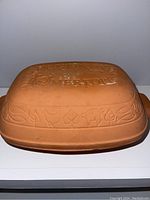 Top and side view of the terracotta bread baker showing embossed Romertopf branding and decorative leaf and flower patterns.