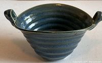 View of the bowl showing the ribbed texture, smooth finish, and artistic dual handles, highlighting the blue-green glaze hues.