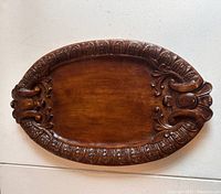 Top view of oval wooden serving tray showing detailed carved border and handles with smooth central surface.