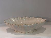 Front angle photo showing white porcelain bowl with scalloped edges and gold trim on an oval shape with pedestal base