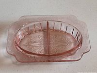 Oval pink Depression glass divided serving bowl with an elaborately embossed floral pattern on the squared outer rim and geometric patterns inside the oval divided sections.