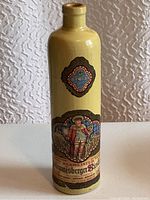 Full view of the tall yellow ceramic stoneware bottle with Beameister label and decorative medallions.