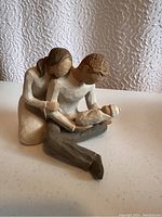 Frontal view of the Willowtree family figurine showing mother embracing father who holds the baby.