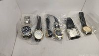 Lot of five watches in plastic bags, displayed side by side showing a variety of strap materials and dial designs.