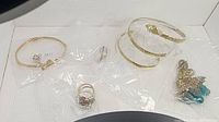 Five-piece jewelry lot arranged against white background with bracelets, ring, earrings visible in plastic bags