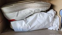 Side and sole view of a white Adidas Stan Smith sneaker showing outsole and box interior with tissue paper.