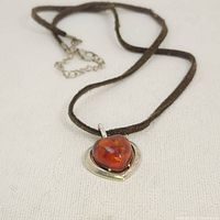 Full view of the amber heart pendant with visible inclusions on a brown cord with silver chain extender.
