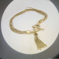 Full view of gold-tone antique lariat necklace showing multi-strand woven design with toggle clasp and tassel pendant
