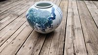 Photo of an antique Korean porcelain vase with detailed blue floral and foliage design placed on a wooden deck.