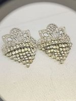 Pair of antique Art Deco shoe clips with filigree and rhinestones arranged in a diamond shape on white fabric background.