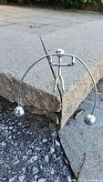 Photo of the silver metal balance ledge figurine resting on a concrete ledge, showing the curved rod with weighted balls and the simplistic human shape.