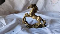Photo of a vintage brass horse figurine showing rearing pose and surface patina on cloth background.
