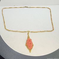 Full view of the necklace laid flat showing the chain and the coral pendant.